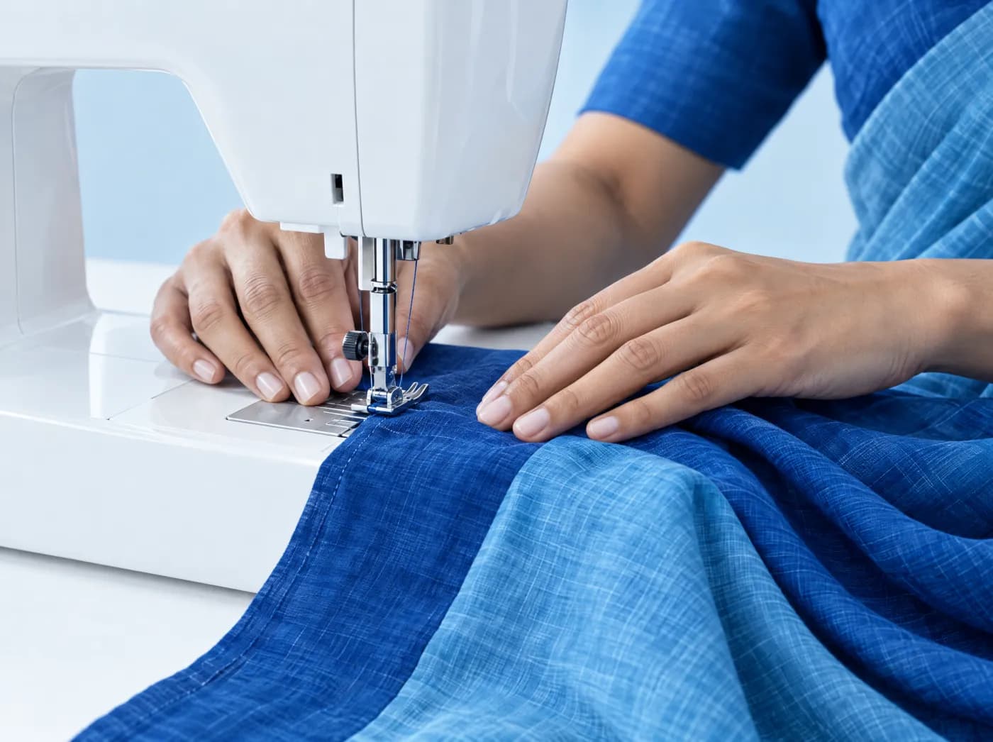 Hands guiding blue cotton under a sewing machine needle