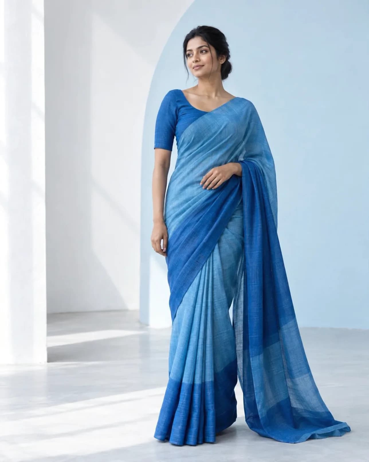 A woman wearing a flowing cerulean blue saree in a light-filled, modern studio